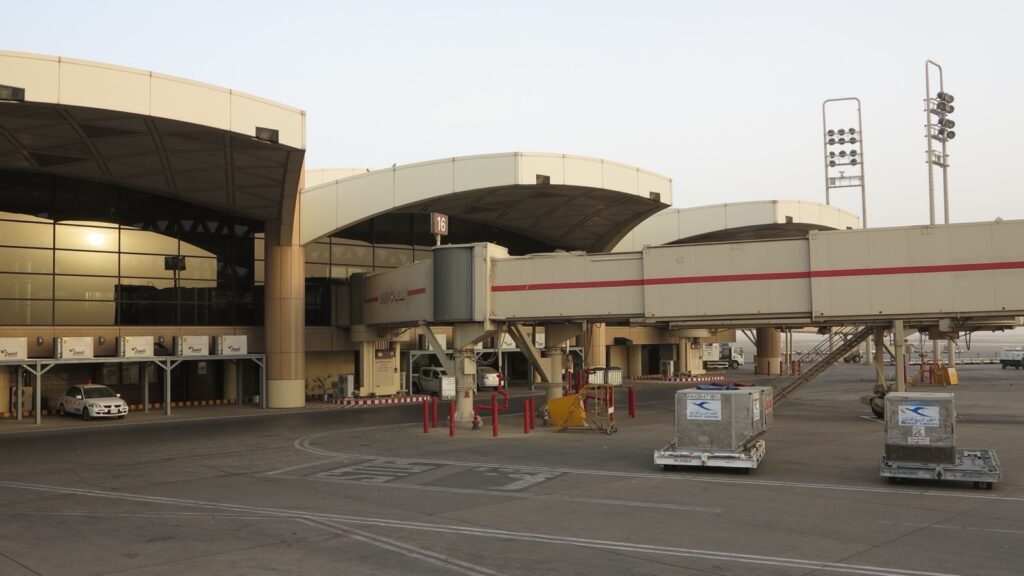Terminal 1 Međunarodnog aerodroma Kralj Halid u Rijadu: zgrada sa lučnim krovovima, avio-mostovi i kontejneri za prtljag na platformi