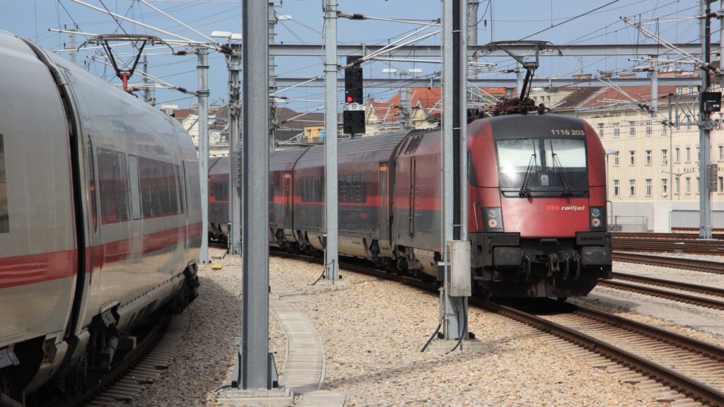 Crveni voz Railjet austrijskih železnica ÖBB izlazi sa Glavne železničke stanice u Beču, levo stoji beli nemački voz ICE