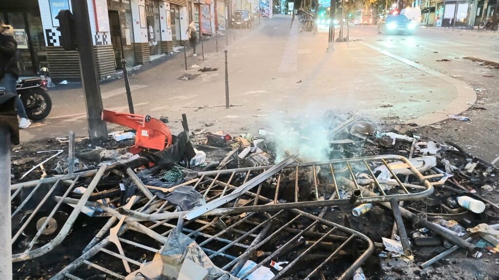 Izgorele metalne ograde i otpad se još dime na trotoaru pariske ulice posle nereda, u pozadini zatvorene radnje