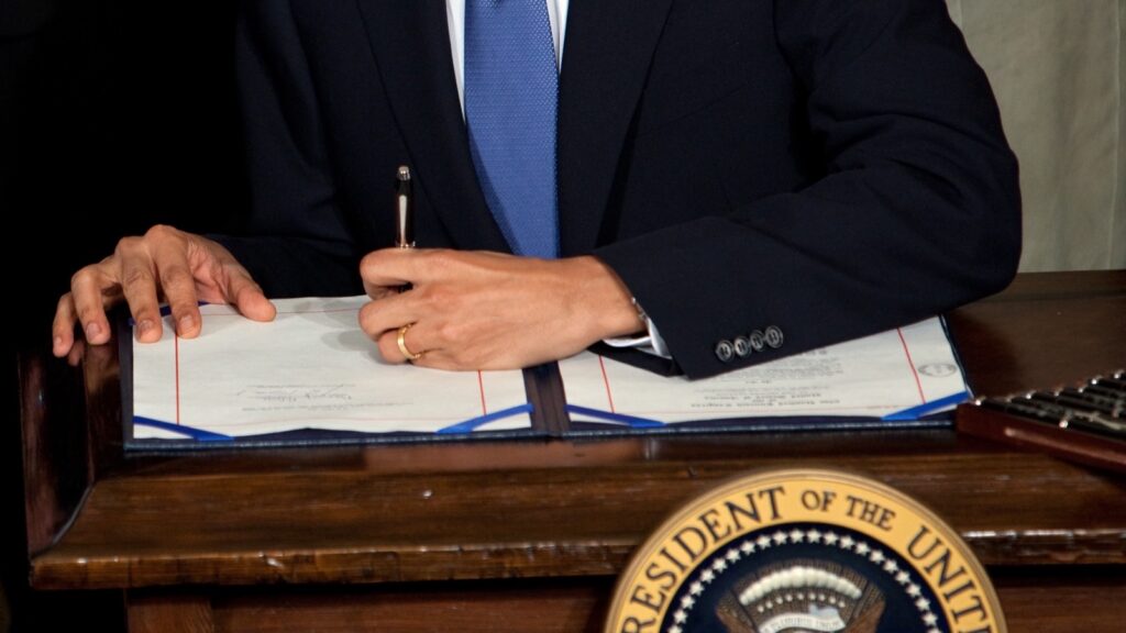 Barak Obama potpisuje zakon o zdravstvenom osiguranju (Obamacare) za stolom sa predsedničkim grbom u Beloj kući, mart 2010.