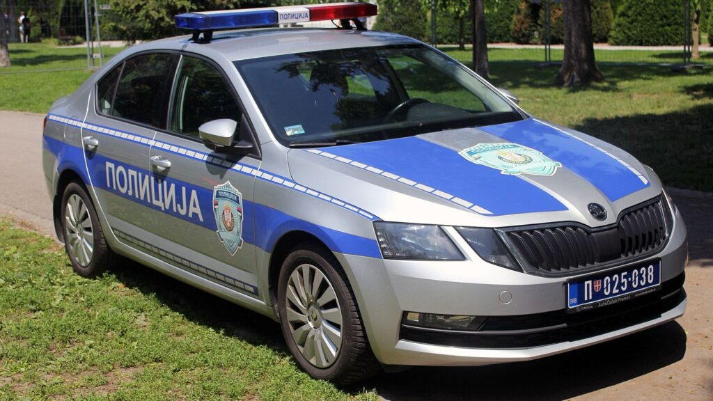 Automobil policije Srbije sa natpisom „Policija“ parkiran na stazi u parku.