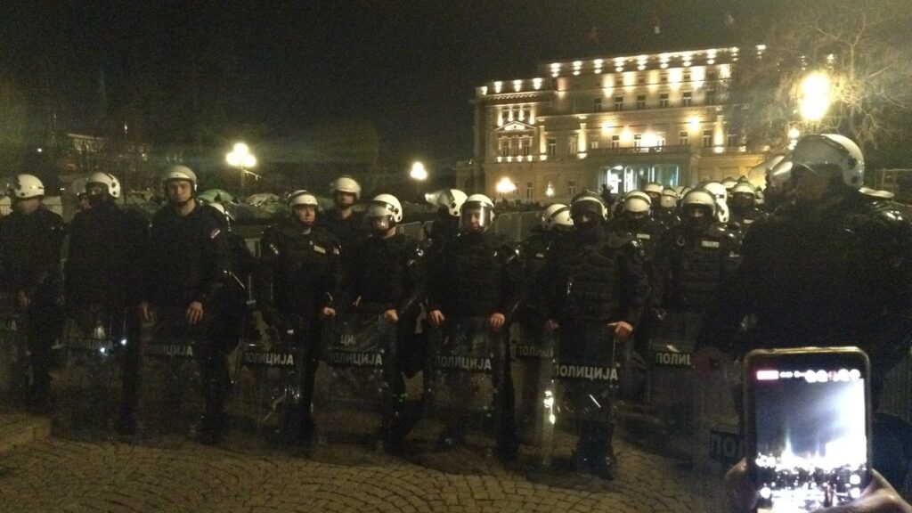 Policijski kordon sa štitovima noću u Beogradu, u prvom planu telefon kojim neko snima policajce