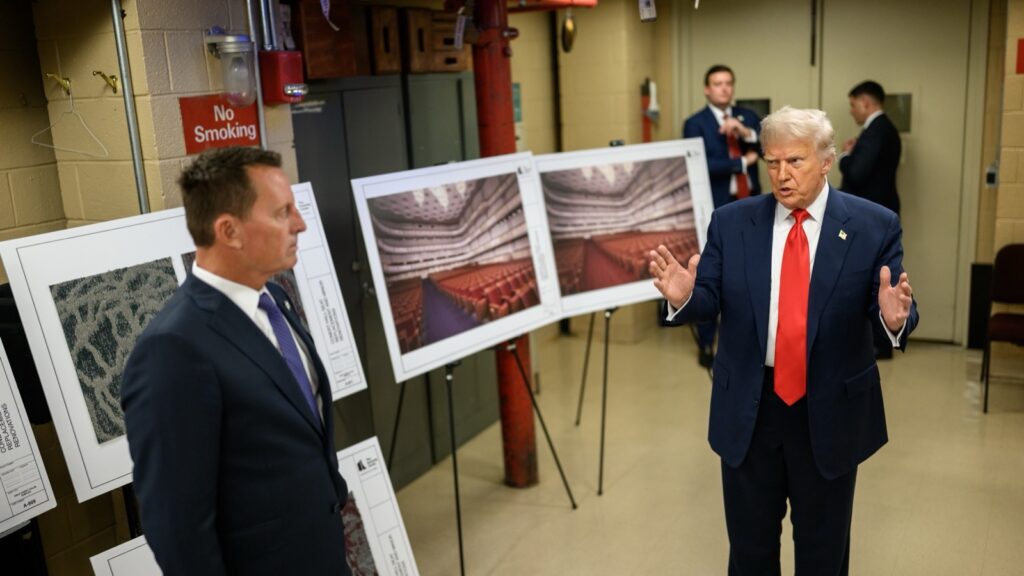 Donald Tramp u tamnom odelu i crvenoj kravati govori Ričardu Grenelu u prostoriji Kenedijevog centra, iza njih panoi sa nacrtima obnove koncertne dvorane